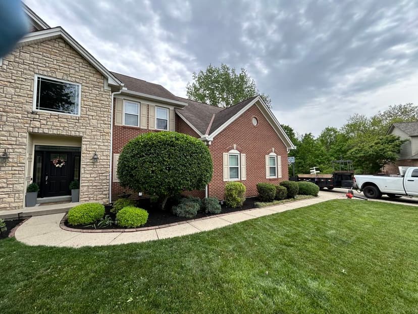 Brick house exterior with landscaped lawn and shrubs, cloudy sky in background.